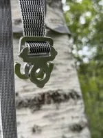 Jord Buckle (olivfärgad variant) på band Jord Buckle i olivfärgat utförande på band mot björkstam